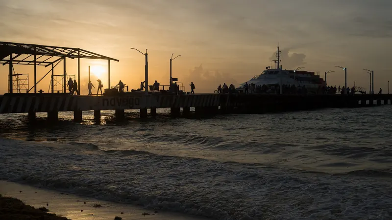 Siluetas de personas en el muelle del ferri de Playa del Carmen mientras sale el sol sobre el Caribe