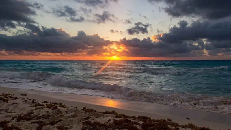 Sol saliendo sobre el mar Caribe entre nubes, visto desde una playa de la Zona Hotelera de Cancún