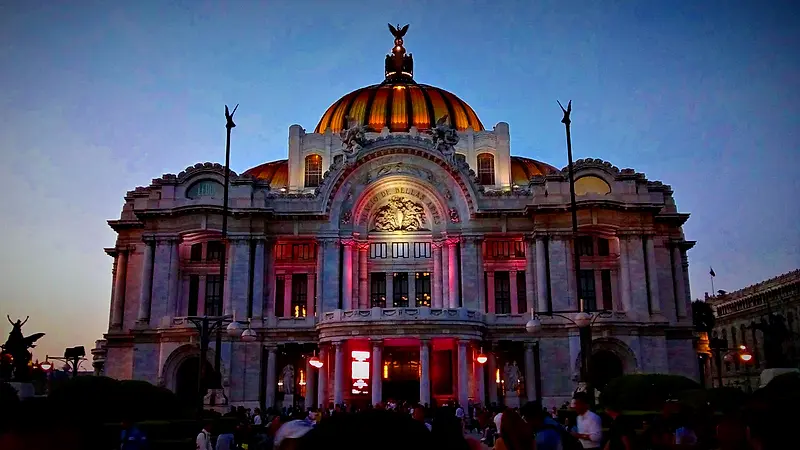 Palacio de Bellas Artes iluminado al caer la tarde, con gente paseando frente a la fachada, en Ciudad de México