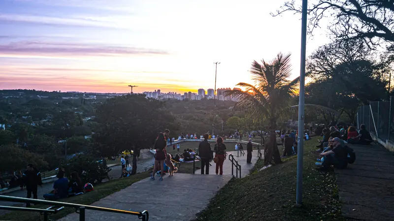 Pessoas no gramado da Praça do Pôr do Sol, em São Paulo, vendo o céu laranja do fim de tarde sobre a Zona Oeste